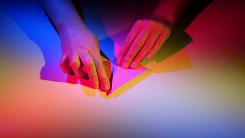 Hands Make Origami With Paper Under Colorful Lighting