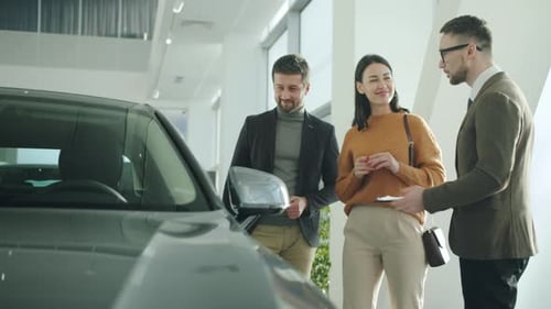 Happy Man and Woman Talking To Car Dealer in Dealership Discussing Automobiles