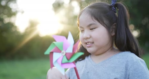 Funny asian girl with colored windmill in the garden