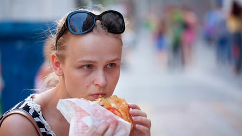 Woman Enjoying Sandwich on City Street Corner