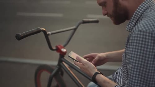 Young Man with Bmx Bicycle Uses His Phone at Sunset on the Street