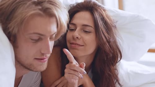 Deux amoureux caucasiens couchés dans leur lit sous une couverture le matin flirtant, s'embrassant en souriant