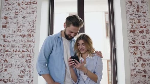 Smiling Couple Sharing a Phone by a Window