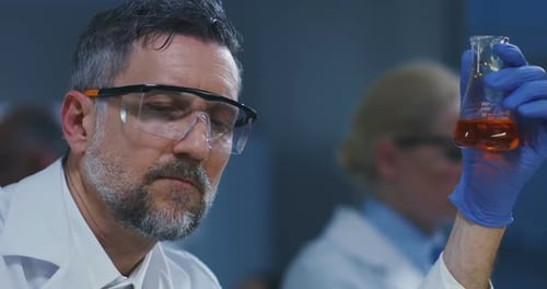 Scientist Examines Flask With Orange Liquid