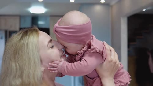 The Mother Turns Her Face to the Baby and Swings the Baby in Her Arms on the Background of a Modern