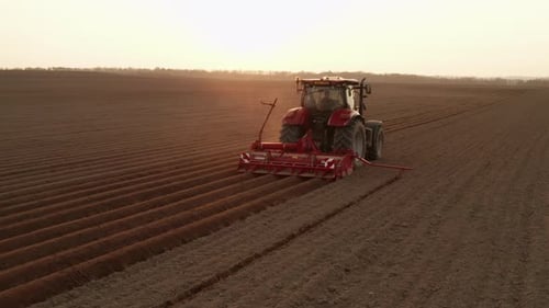 Red Tractor Working in Agriculture Field at Sunset