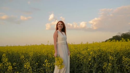 Young Redhaired Woman Walking in the Middle of a Blooming Field and Smiling Slow Motion