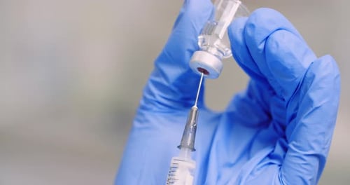 Syringe drawing liquid from glass medicine vial