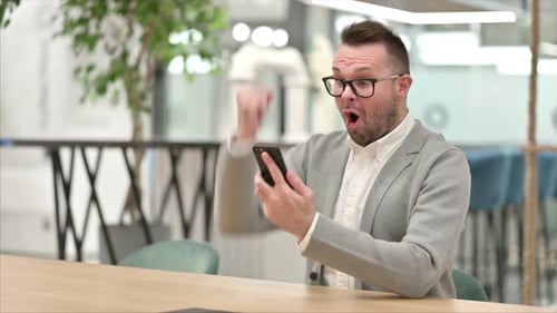 Excited Man Celebrating Success with Mobile Phone in Office