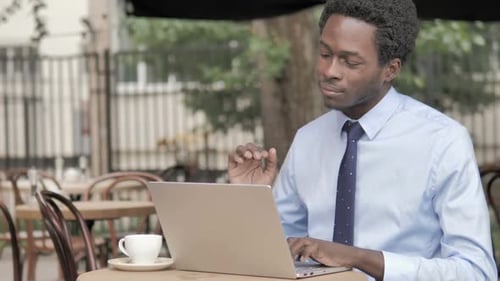 Coughing African Businessman Working on Laptop in Outdoor Cafe