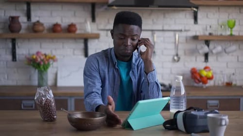 Young Man Talking on the Phone in Slow Motion Sitting at Kitchen Table in Home Office