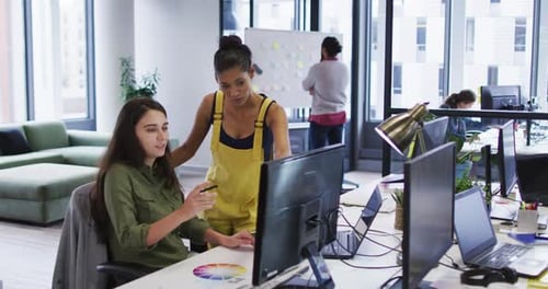 Zwei verschiedene Arbeitskollegen schauen auf Computermonitor und sprechen
