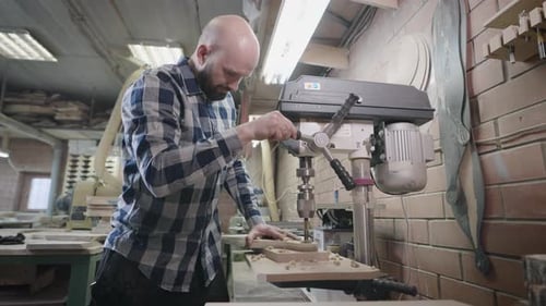 An Experienced Carpenter Works with a Drilling Machine in His Workshop
