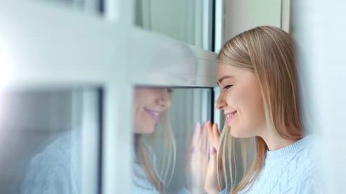Closeup Carefree Smiling Young Woman Looking on Window Touching Glass By Hand Side View