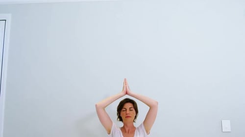 Woman Meditating with Hands Above Head in Bedroom