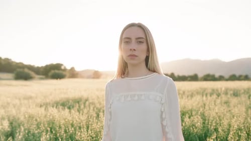 Portrait shot of young woman without countenance in face looking into camera standing on farm field