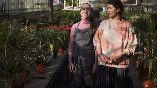 Two Women Walking Through Greenhouse Discussing Plants