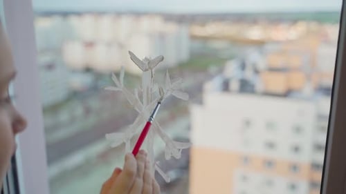 Child draw snowflake on window with paints close-up. Caucasian female person decorate living room
