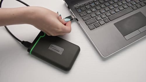Modern Technologies a Young Woman Inserts a Portable Hard Disk Into a Laptop on a Light Background