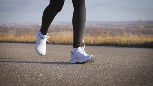 Nahaufnahme von Frauenbeinen beim Laufen auf Asphaltstraße
