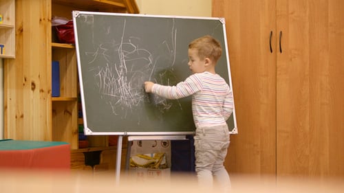 Young Child Drawing on Chalkboard in Classroom
