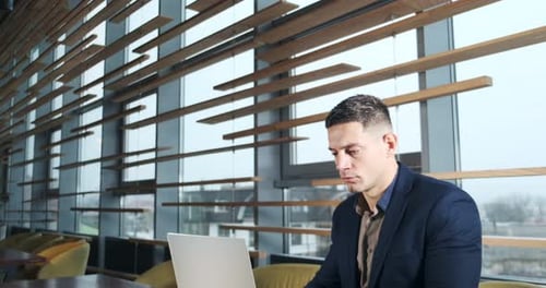 Concerned Man Working on Laptop Computer and Looking Away Thinking Solving Problem at Office