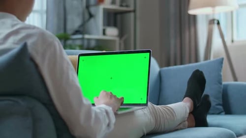 Man Typing On Green Screen Laptop While Lying On Sofa In The Living Room