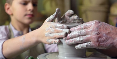 Boy and Adult Shaping Clay on Pottery Wheel