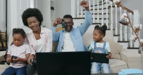 Familia con niños sentados en el suave sofá de casa y disfrutando de un videojuego en una computadora portátil