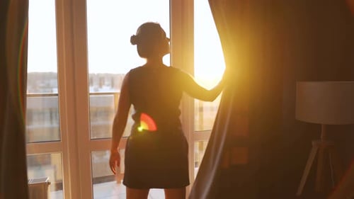 Woman Opens Curtains To Let Sunlight Into the Room