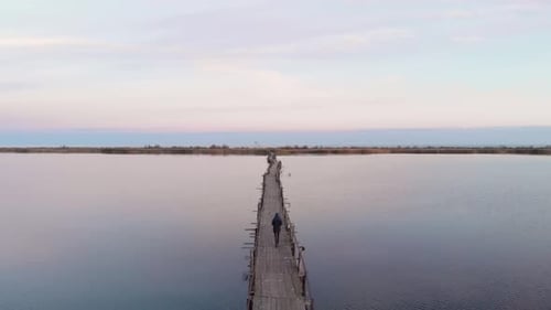Mann geht auf Holzbrücke durch den See mit ruhigem klarem Wasser.
