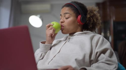 Woman Eats Apple While Using Laptop Indoors