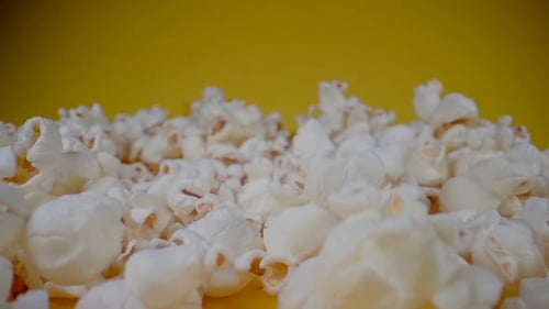 Nahaufnahme Dolly Shot von fallendem süßem Popcorn vor gelbem Hintergrund in Zeitlupe