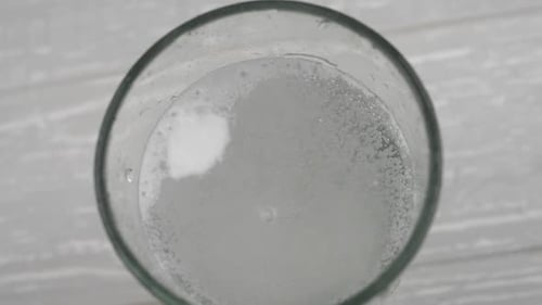 Effervescent aspirin tablet dropping to glass of water. Slow motion fizzy pill falls and dissolves w