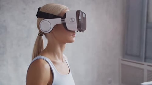 Young and sporty girl in sportswear is doing exercises at home using virtual reality helmet.
