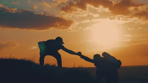Silhouette of Helping Hand Between Two Climber. Two Hikers on Top of the Mountain, a Man Helps a Man