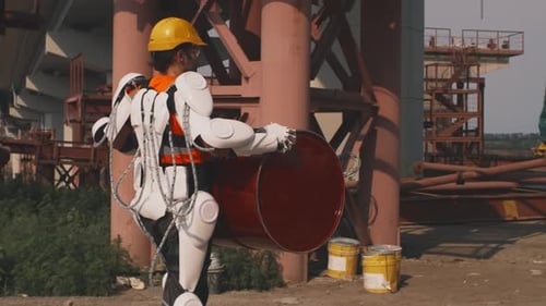 Man With Exoskeleton Carries Barrel on Construction Site