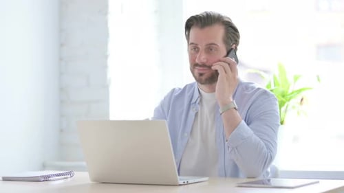 Man Talking on Phone at Desk with Laptop