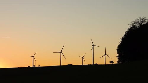 Wind Turbines Silhouetted Against Sunrise in Rural Setting