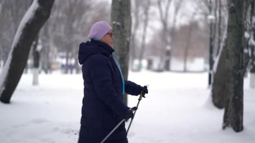 Active Senior Woman Nordic Walking in Snowy Park