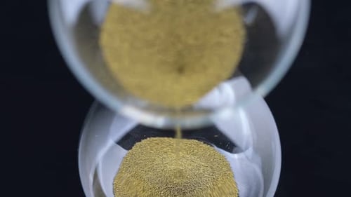 An Hourglass Made of Yellow Metal Shavings Passes Through a Funnel Symbolizing the Concept of Time