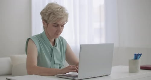Mature Woman Typing on Laptop at Desk