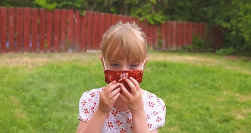 Young Girl Adjusting Mask Outdoors on Lawn