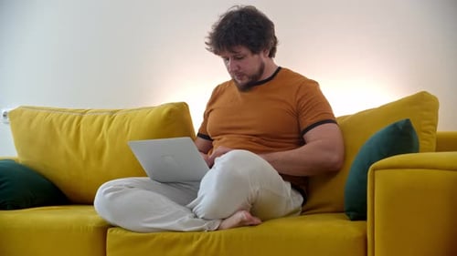 Young Adult Using Laptop on Yellow Sofa