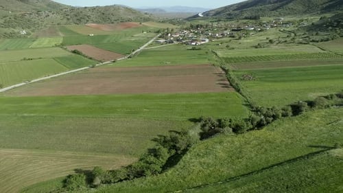 Aerial view of grass fields surrounded by vegetation and hills.