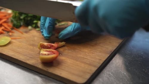 Gloved Hands Chopping Tomato on Wooden Board