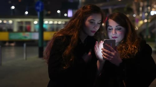Two Women Using Phone at Night in City