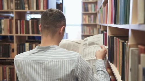 A young man in the library reads the news from the newspaper.