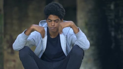 Trauriger afroamerikanischer Teenager setzt Kapuze auf und sitzt allein auf der Straße