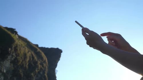 Hands Using Cellphone in Front of Rocky Cliff